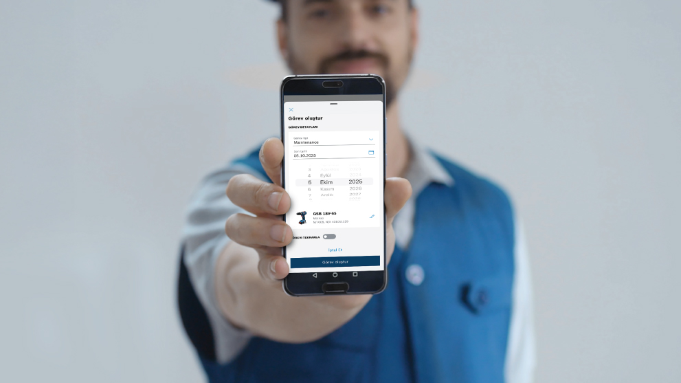 Một người đàn ông giơ chiếc điện thoại thông minh có ứng dụng hiển thị chi tiết công việc. Anh ta mặc áo sơ mi màu xanh dương.