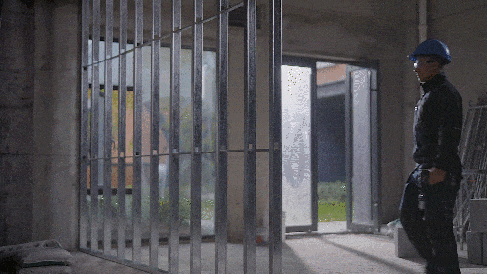 Một công nhân đội mũ bảo hiểm màu xanh đi qua một công trình xây dựng với khung kim loại.