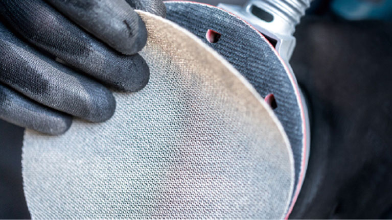 Hai bàn tay đeo găng tay đen cầm một bánh mài.