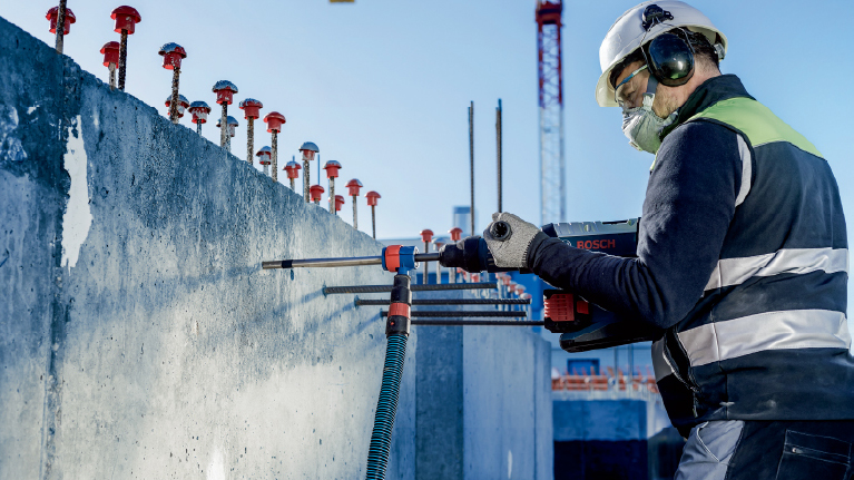 Một công nhân sử dụng dụng cụ Bosch đang làm việc trên bức tường bê tông tại công trường xây dựng.