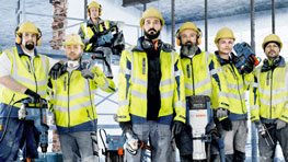 Sáu công nhân xây dựng đội mũ bảo hiểm màu vàng và mặc áo an toàn đang đứng trên công trường xây dựng.