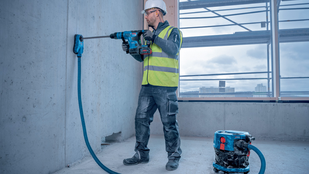 Một người đàn ông đội mũ bảo hiểm và áo chống đạn đang khoan vào bức tường bê tông.