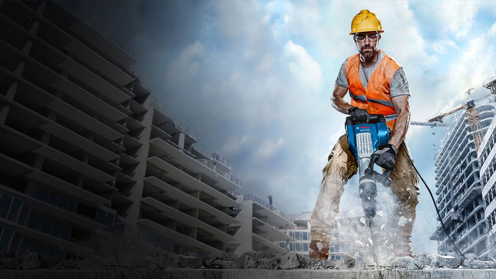 Một người đàn ông đội mũ bảo hiểm và mặc áo vest màu cam đang làm việc với chiếc búa Bosch.