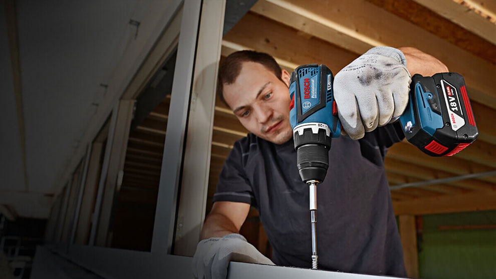 Một người đàn ông đang sử dụng máy khoan không dây Bosch Professional để lắp ráp một thanh kim loại.