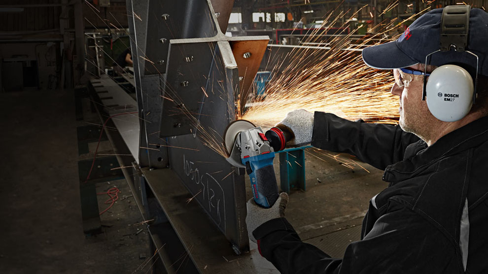 Một người đàn ông đang cắt kim loại bằng dụng cụ Bosch màu xanh. Tia lửa bắn ra.