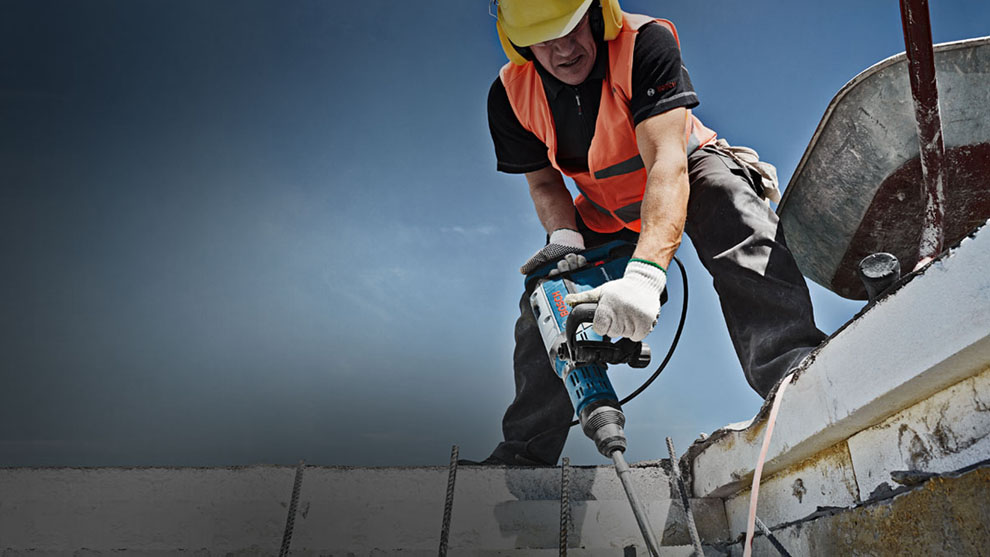 Người thợ thủ công mặc áo an toàn với máy khoan búa Bosch trên công trường xây dựng.