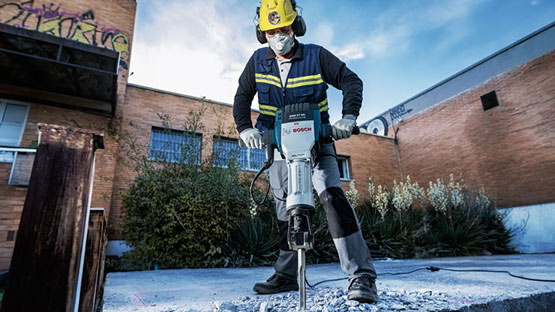 Xây dựng Một công nhân đang sử dụng búa Bosch để làm việc trên bê tông ngoài trời.