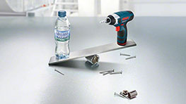Một tua vít không dây chuyên nghiệp của Bosch, một bình nước và ốc vít trên kim loại.