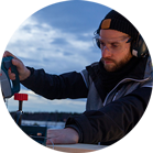 Một người đàn ông đeo tai nghe đang cắt gỗ bằng cưa Bosch ngoài trời.