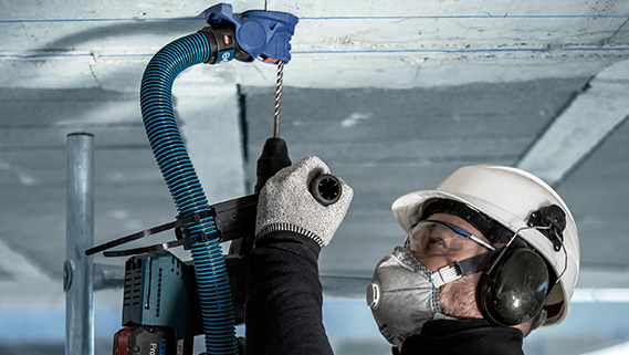 Một thợ thủ công đội mũ bảo hiểm và đeo tai nghe bảo vệ đang khoan trên trần.