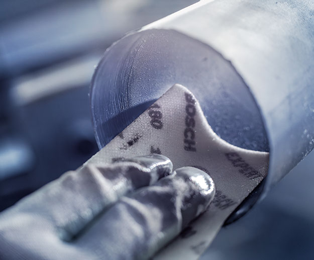 Một bàn tay giữ giấy nhám Bosch trên một mảnh kim loại tròn.