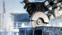 Một bàn tay đeo găng tay cầm một máy mài góc đang xử lý bê tông.